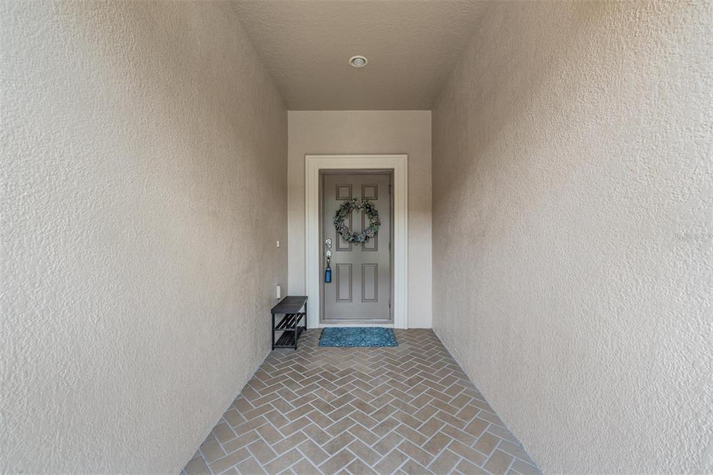 A covered entryway features a gray front door with a wreath and herringbone-patterned tile flooring — 12039 GREENGATE DRIVE, HUDSON, FL