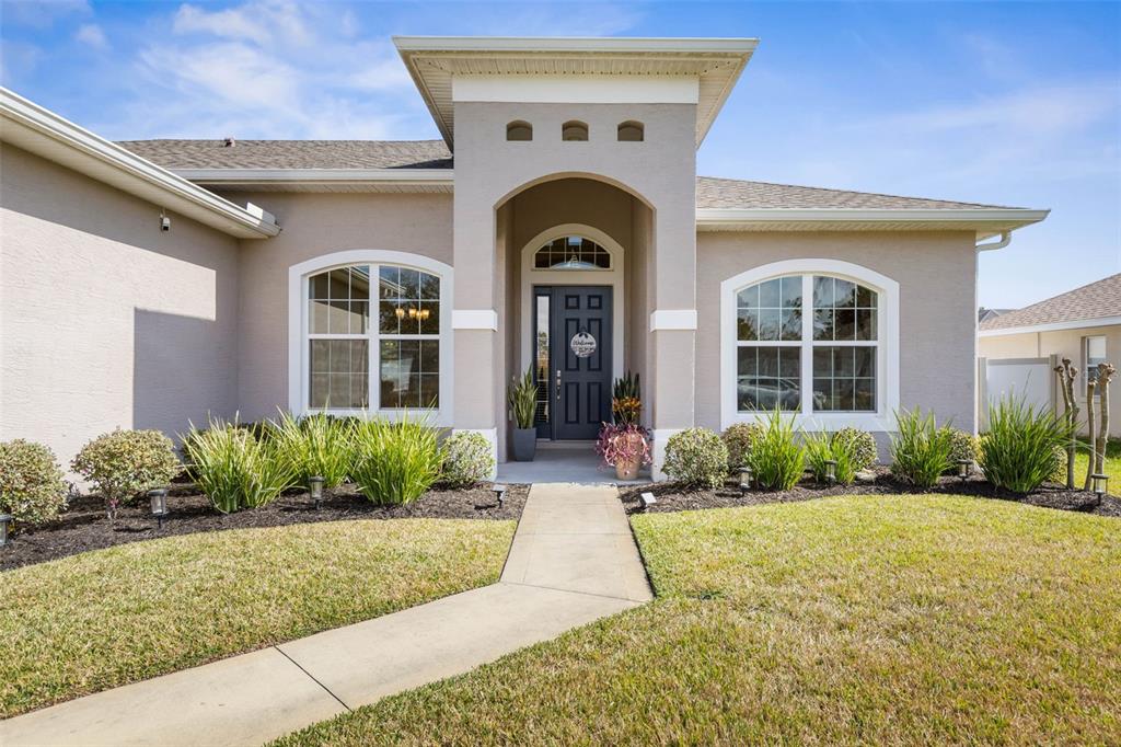 The exterior of a single-story house features a tan stucco facade, arched windows, and a walkway — 15 FAIRCHILD LANE, PALM COAST, FL