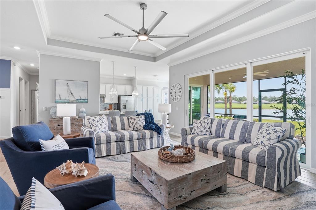 A coastal-style living room features striped sofas, blue armchairs, a wooden coffee table, and lake views — 15073 RIVER BIRCH COURT, PUNTA GORDA, FL