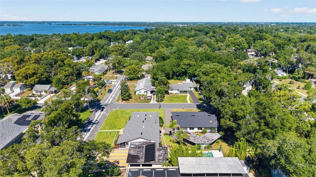 An aerial view shows a residential neighborhood with houses, lush trees, and a distant lake — 205 E 10TH AVENUE, MOUNT DORA, FL
