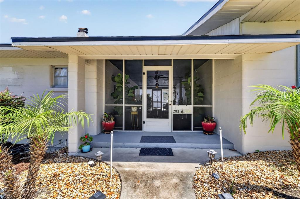 The exterior of a house features a covered entryway with a screened-in porch and landscaping — 205 E 10TH AVENUE, MOUNT DORA, FL