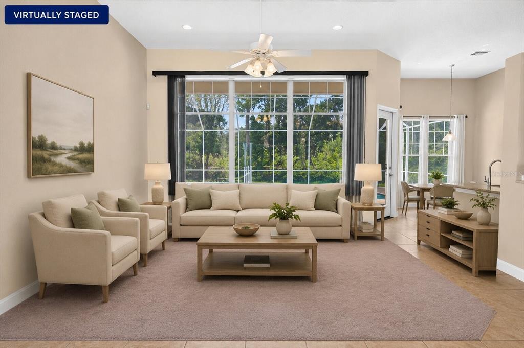 This virtually staged living room features a beige sofa, two armchairs, and large windows — 180 BLACK HICKORY WAY, ORMOND BEACH, FL