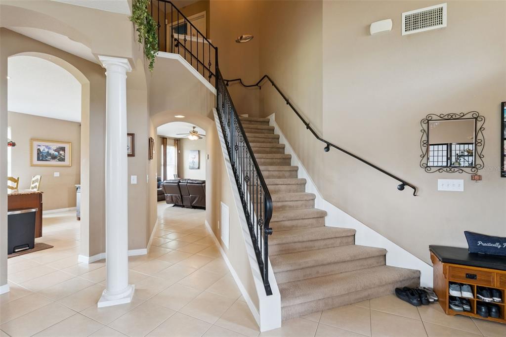 An entryway features a carpeted staircase with a black metal railing and beige tile flooring — 3636 BRISTOL COVE LANE, ST CLOUD, FL