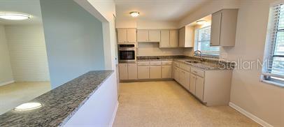 A kitchen features light-colored cabinets, granite countertops, and a pass-through window to the dining area — 1512 PICARDY CIRCLE, CLEARWATER, FL