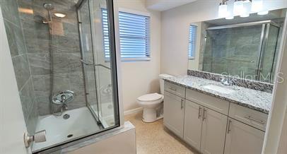 A bathroom features a glass-enclosed shower-tub combination, a vanity with granite countertops, and a toilet — 1512 PICARDY CIRCLE, CLEARWATER, FL