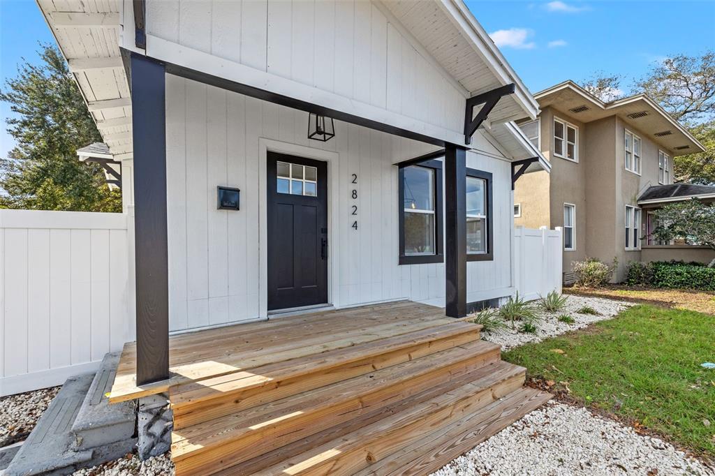 A white house exterior features a wooden porch with steps and a dark front door — 2824 5TH AVENUE N, ST PETERSBURG, FL