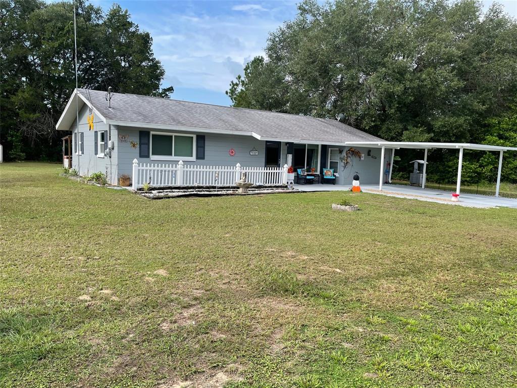 A single-story house with gray siding, a white picket fence, and an attached carport — 21332 SW RAINBOW LAKES BOULEVARD, DUNNELLON, FL