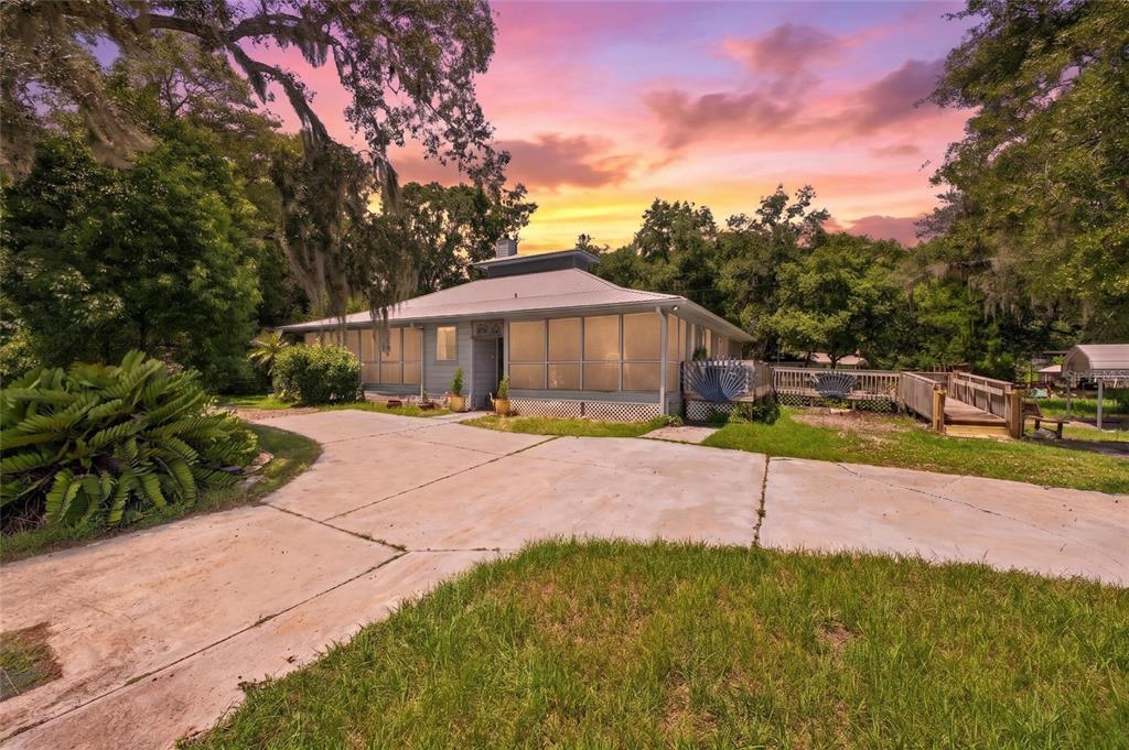 A single-story house with a screened-in porch and a concrete driveway under a sunset sky — 25717 TROON AVENUE, SORRENTO, FL