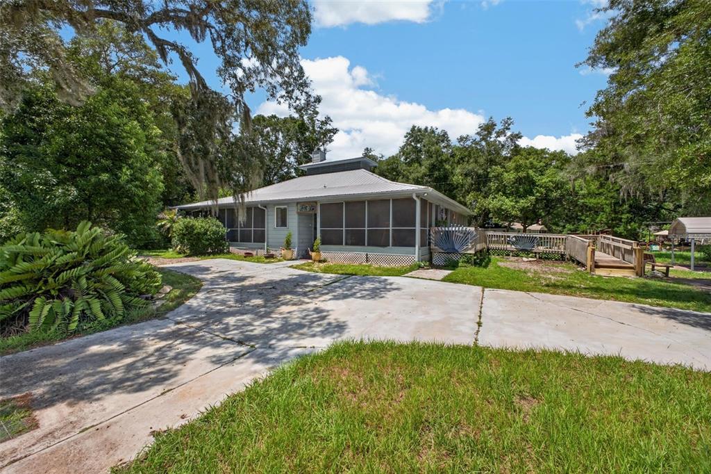 A single-story house with a screened porch and a concrete driveway sits among trees — 25717 TROON AVENUE, SORRENTO, FL