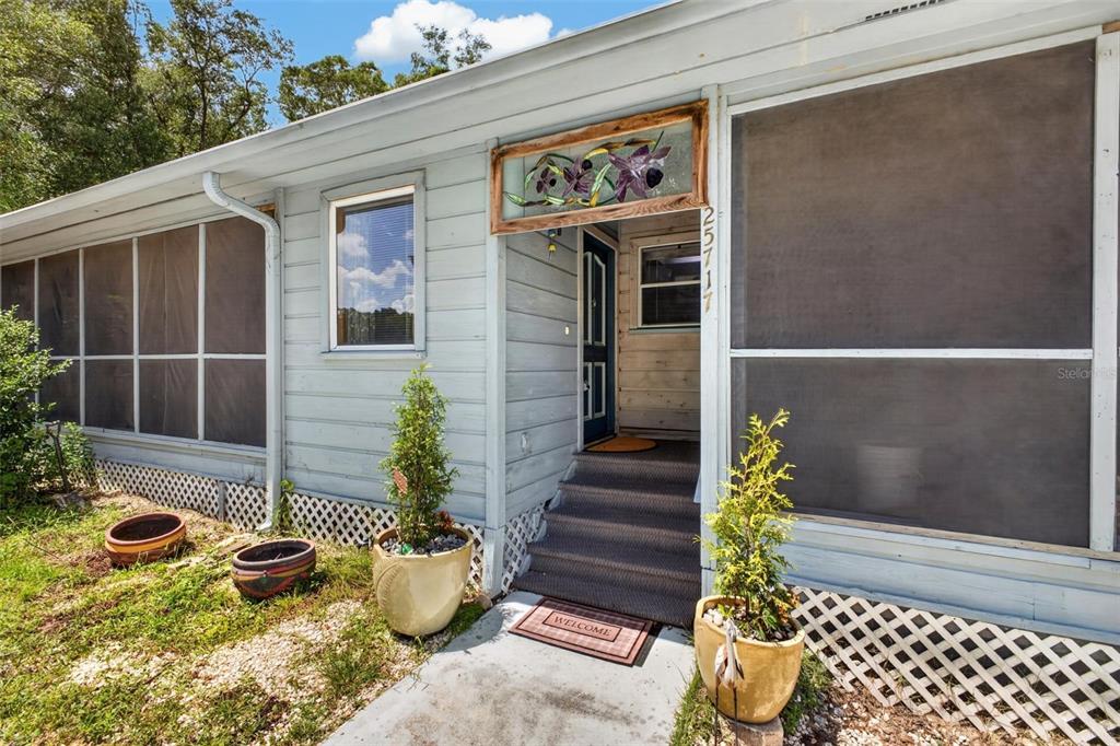 The exterior of a light blue home features a screened-in porch and a front entryway — 25717 TROON AVENUE, SORRENTO, FL