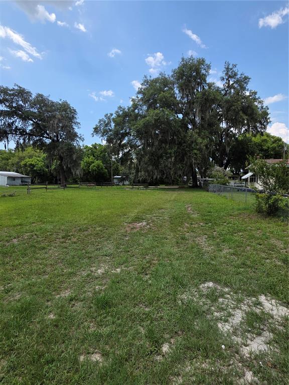 A large, grassy lot features several mature oak trees under a partly cloudy sky — 36749 JUDEE DRIVE, ZEPHYRHILLS, FL