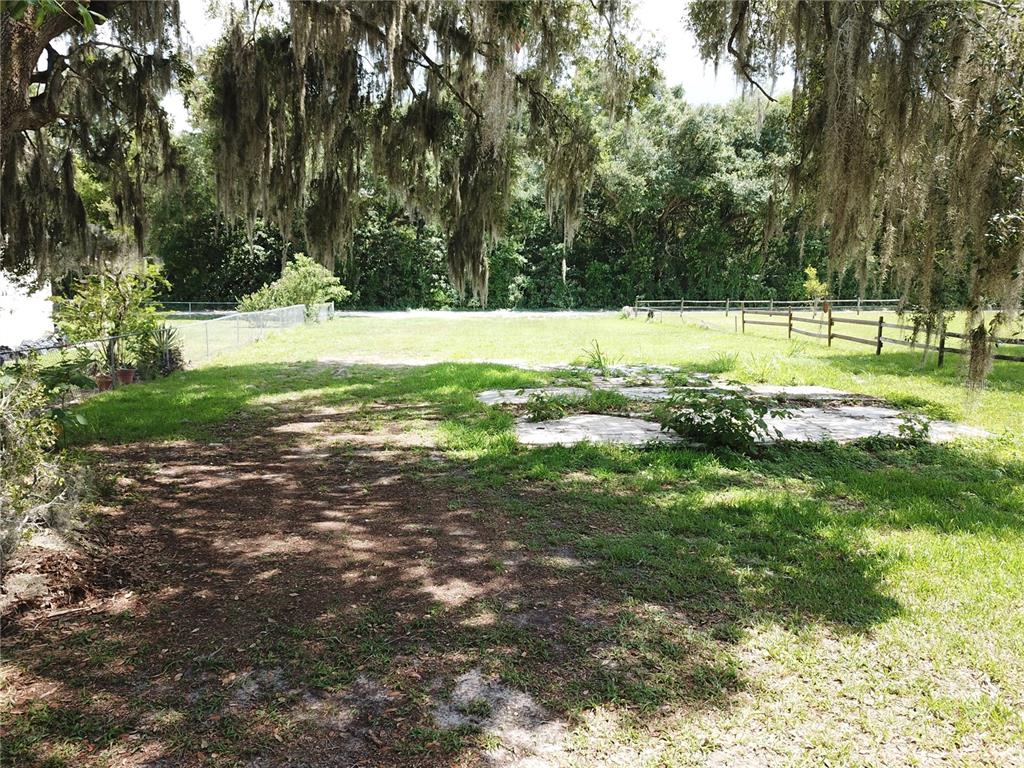A grassy, tree-shaded lot features a concrete slab foundation and a wooden fence — 36749 JUDEE DRIVE, ZEPHYRHILLS, FL