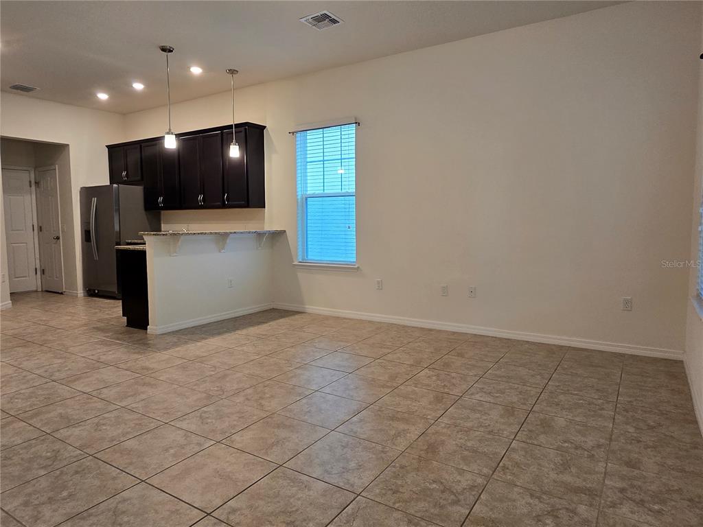 An open-concept kitchen with dark cabinets and a breakfast bar overlooks a tiled living area — 9349 TYRELLA PINE TRAIL, WINTER GARDEN, FL
