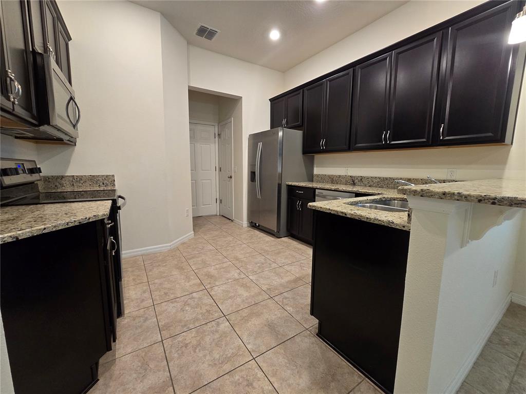A kitchen features dark wood cabinets, granite countertops, stainless steel appliances, and tiled flooring — 9349 TYRELLA PINE TRAIL, WINTER GARDEN, FL