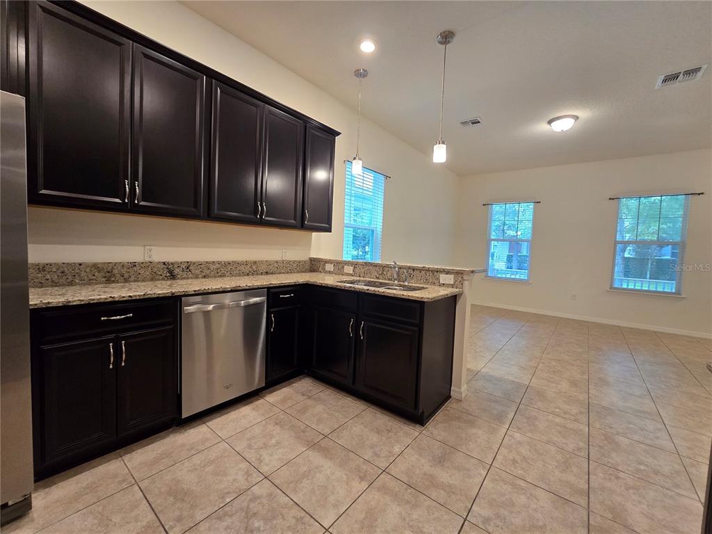 A kitchen with dark cabinets, granite countertops, stainless steel appliances, and tile flooring — 9349 TYRELLA PINE TRAIL, WINTER GARDEN, FL