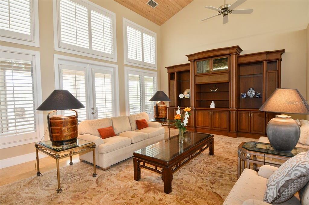 A living room with high ceilings, large windows, a beige sofa, and a wooden entertainment center — 630 N RIVER ROAD, VENICE, FL