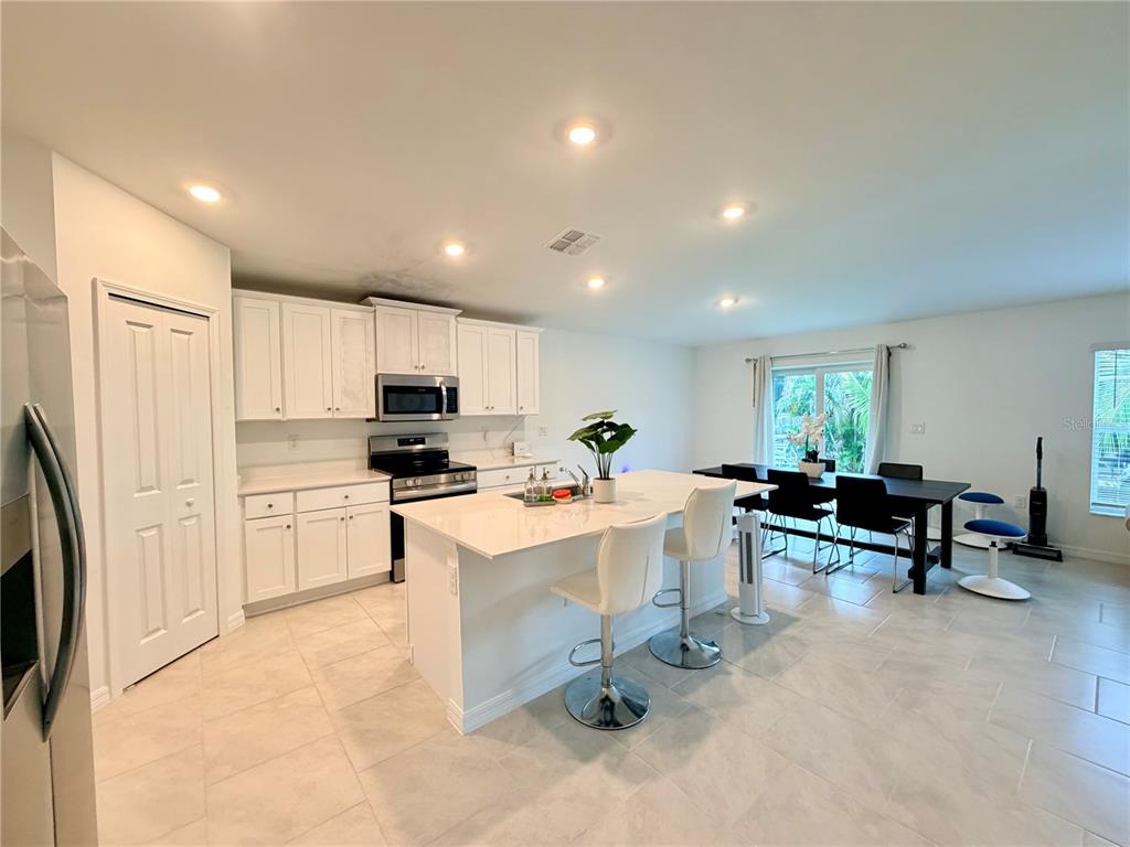 A kitchen with white cabinets, a central island with bar stools, and an adjacent dining area — 1026 DEWHURST STREET, PORT CHARLOTTE, FL