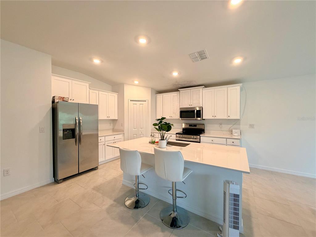 A modern kitchen features white cabinetry, stainless steel appliances, and a central island with stools — 1026 DEWHURST STREET, PORT CHARLOTTE, FL