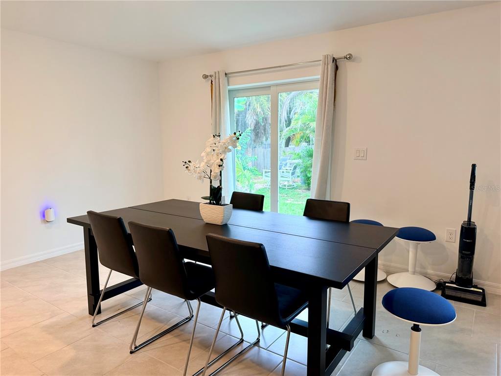A dining room features a black table with matching chairs, tile flooring, and sliding glass doors — 1026 DEWHURST STREET, PORT CHARLOTTE, FL