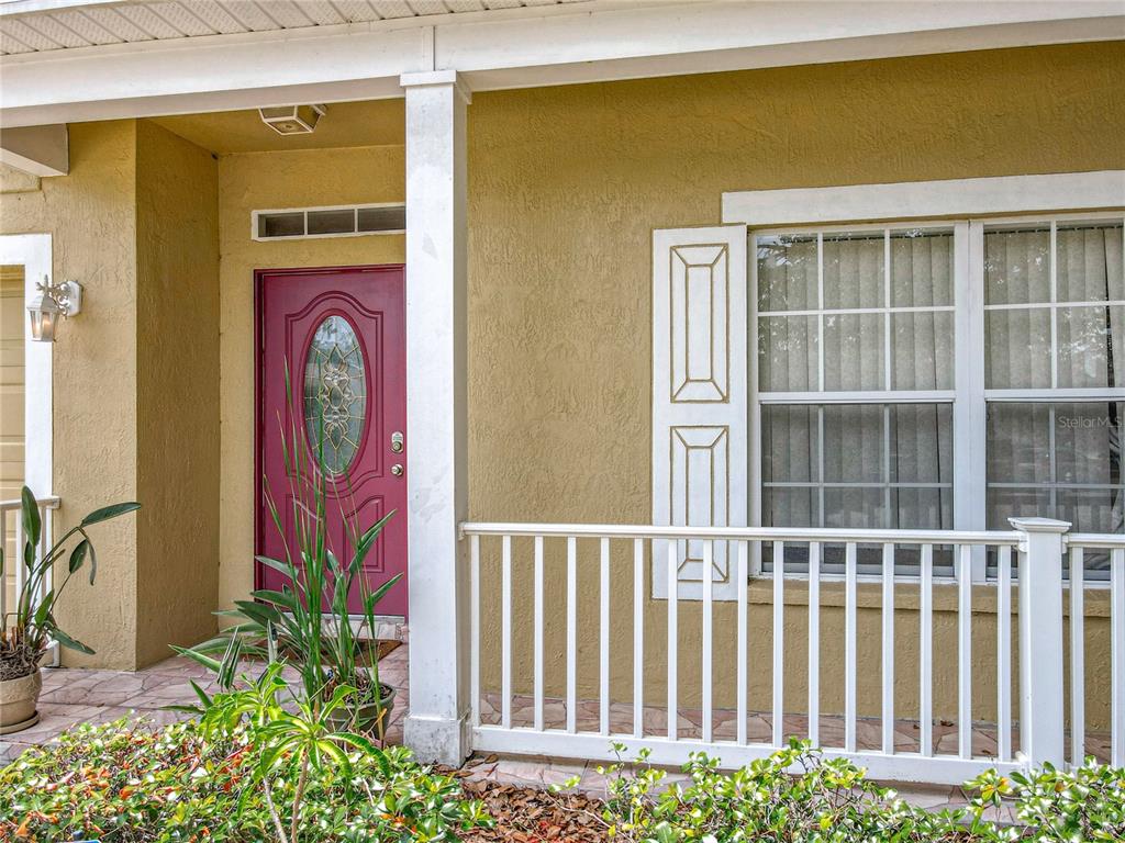 A covered front porch features a red door, white railing, and a window with shutters — 7939 RIFFLE LANE, ORLANDO, FL