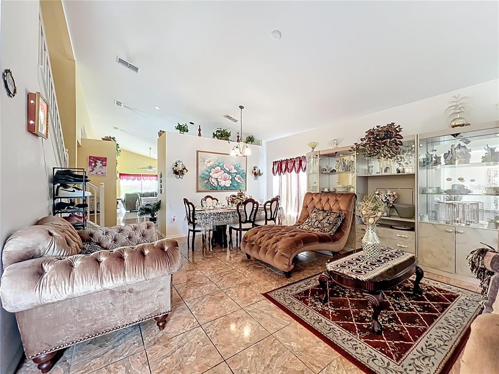 A living and dining area features tiled floors, tufted velvet furniture, and a glass display cabinet — 7939 RIFFLE LANE, ORLANDO, FL