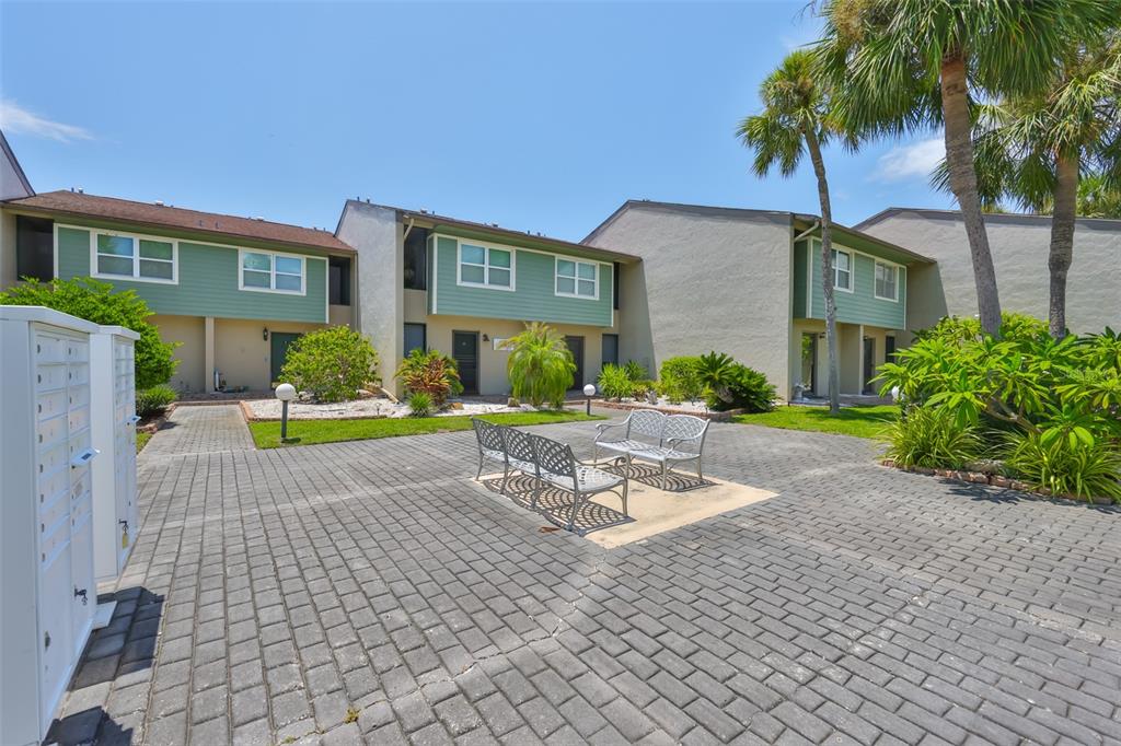 A paved courtyard features metal benches in front of multi-story townhomes with green siding — 1028 APOLLO BEACH BOULEVARD UNIT 8, APOLLO BEACH, FL