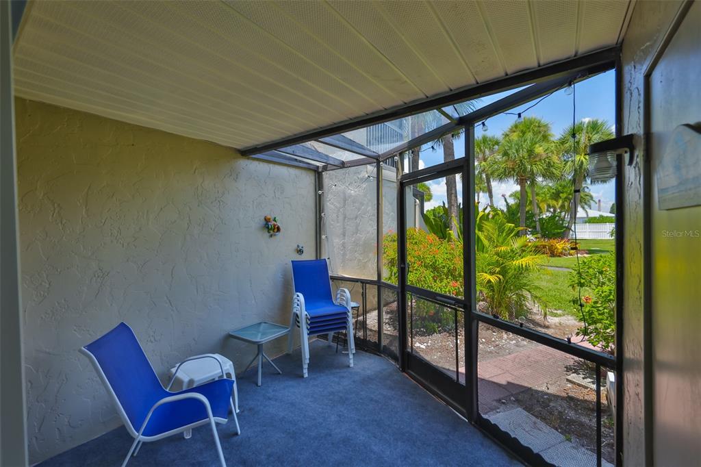 A screened-in patio features blue chairs, a small table, and a view of palm trees — 1028 APOLLO BEACH BOULEVARD UNIT 8, APOLLO BEACH, FL