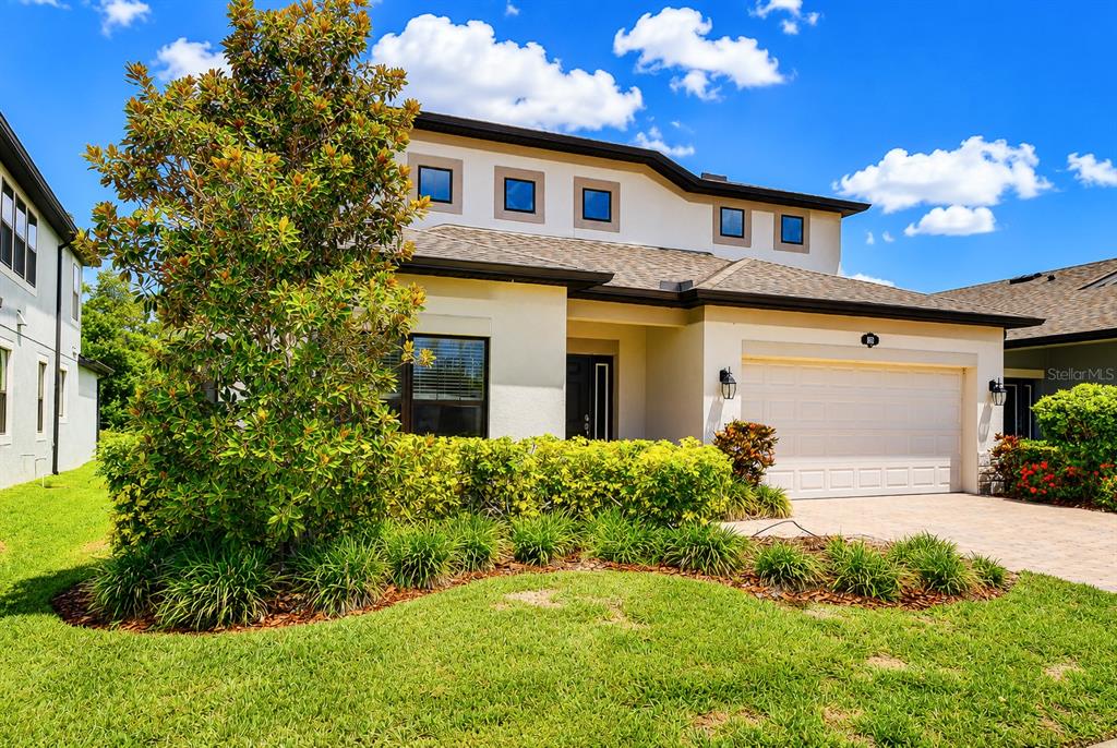 A two-story house with a beige stucco exterior, a two-car garage, and front landscaping — 1621 LEAF FLOWER LANE, LUTZ, FL