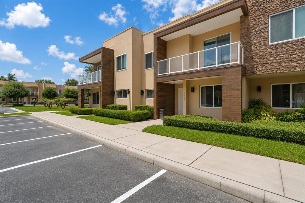 A two-story apartment building exterior features tan stucco, stone accents, balconies, and a parking lot — 3202 BRASILIA AVENUE, KISSIMMEE, FL