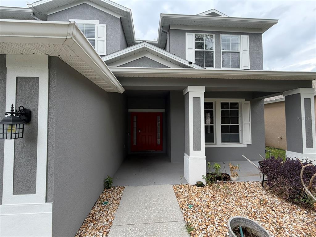 A gray two-story house features a covered entryway with a red front door and stone landscaping — 2549 BALFORN TOWER WAY, WINTER GARDEN, FL