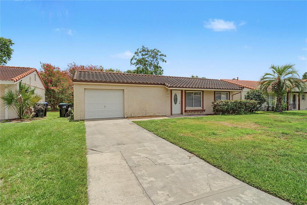 A single-story house with a tan stucco exterior, a tiled roof, and a front lawn — 10145 BLUFF COURT, ORLANDO, FL