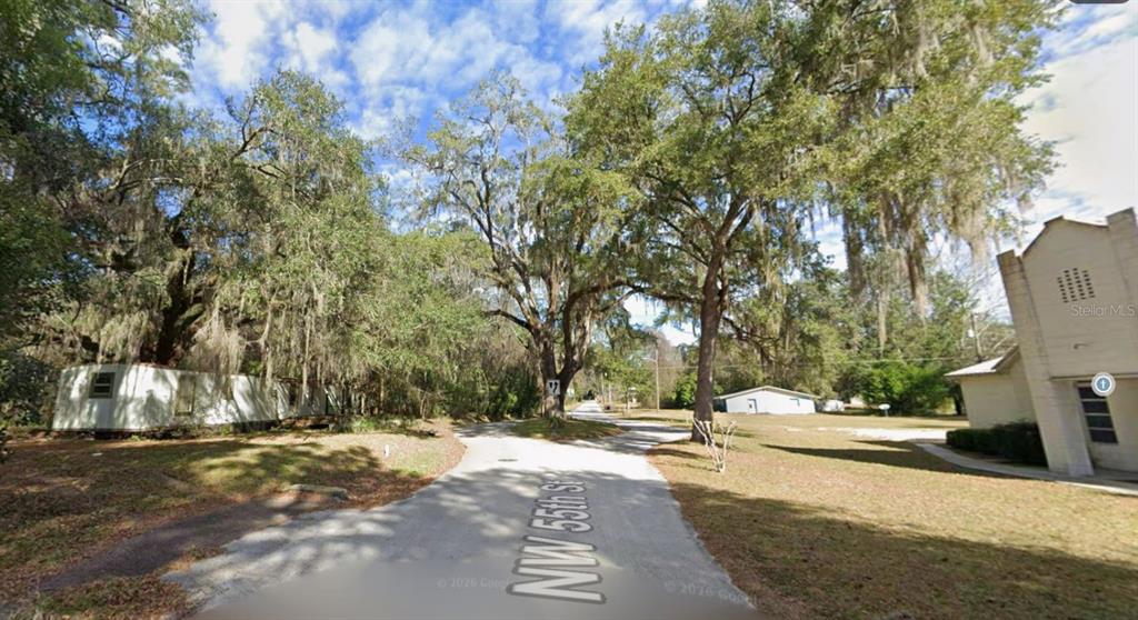 A street view shows a paved road flanked by trees, a mobile home, and a building — NW 55TH STREET, GAINESVILLE, FL