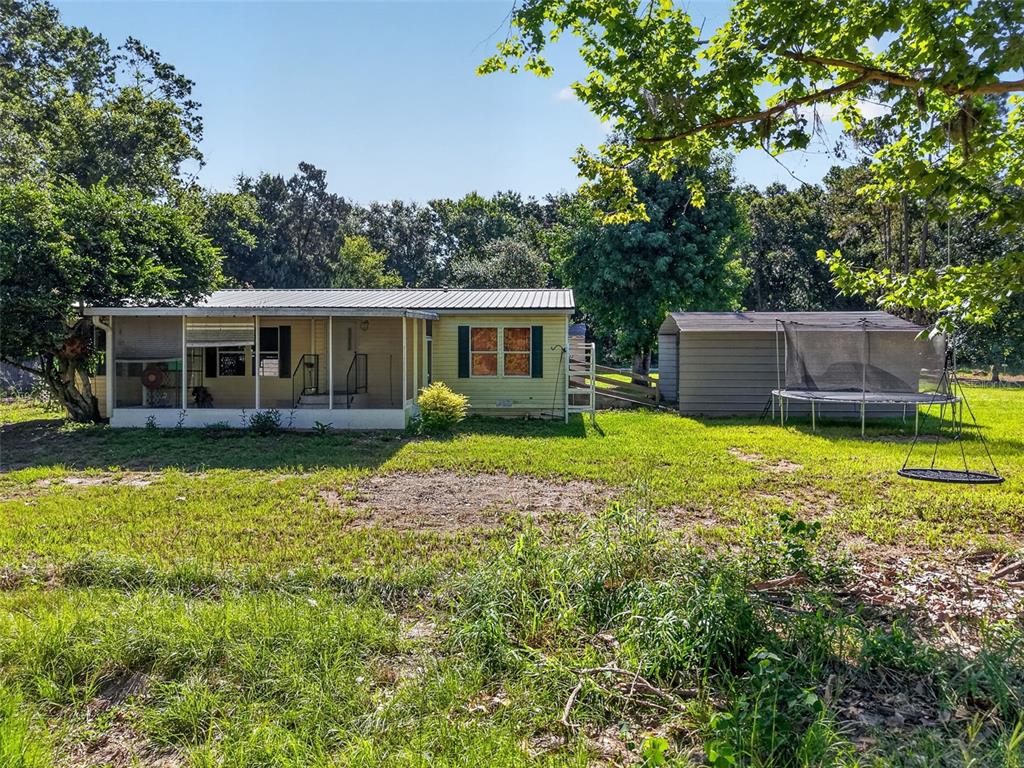 A yellow house with a screened-in porch stands next to a shed and a trampoline — 24301 JEFFERSON ST, ASTATULA, FL