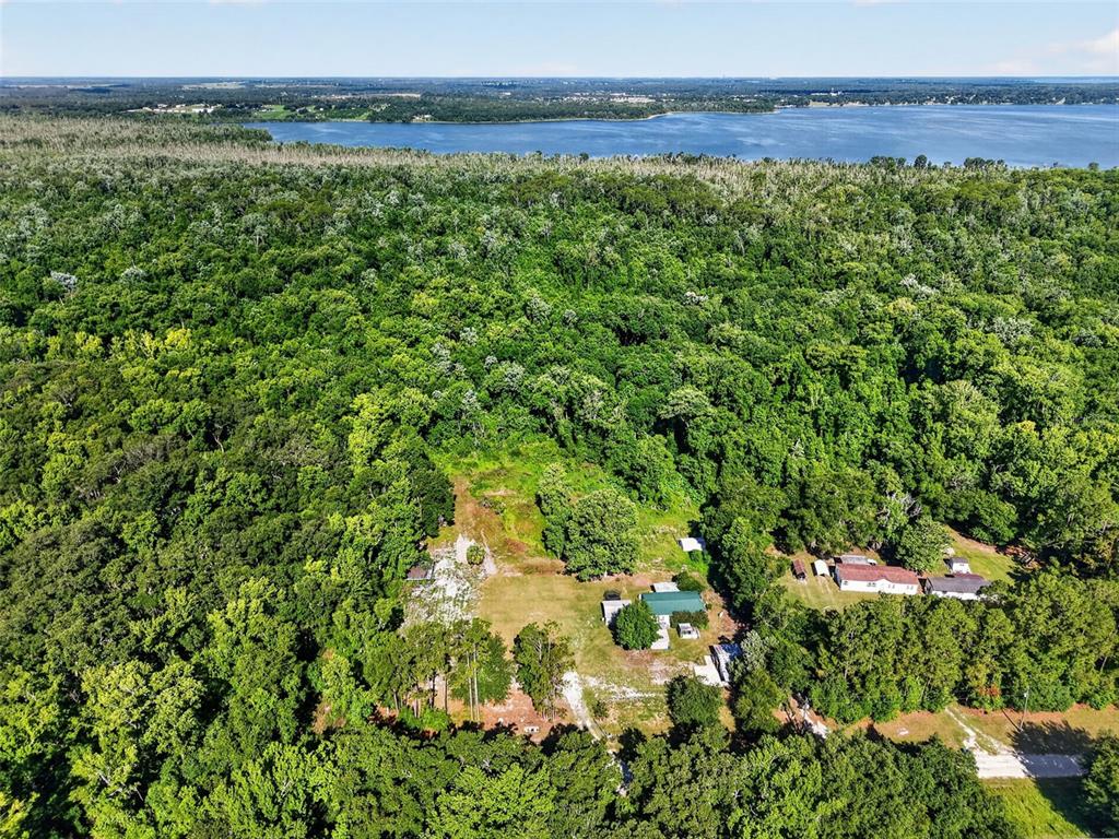 An aerial view shows a house and outbuildings surrounded by dense forest near a lake — 24301 JEFFERSON ST, ASTATULA, FL