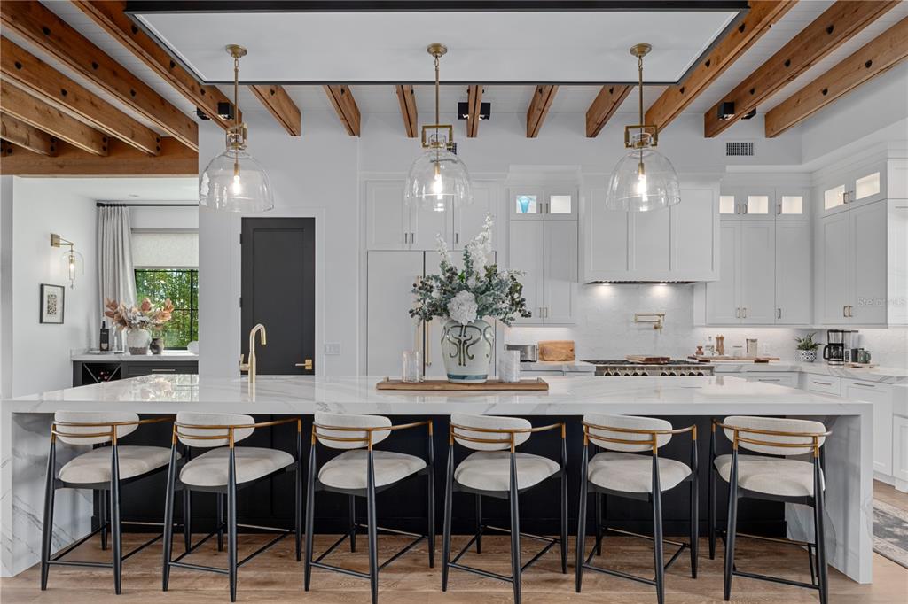 A modern kitchen features a large marble island with six stools under exposed wooden beams — 692 GLADWIN AVENUE, FERN PARK, FL