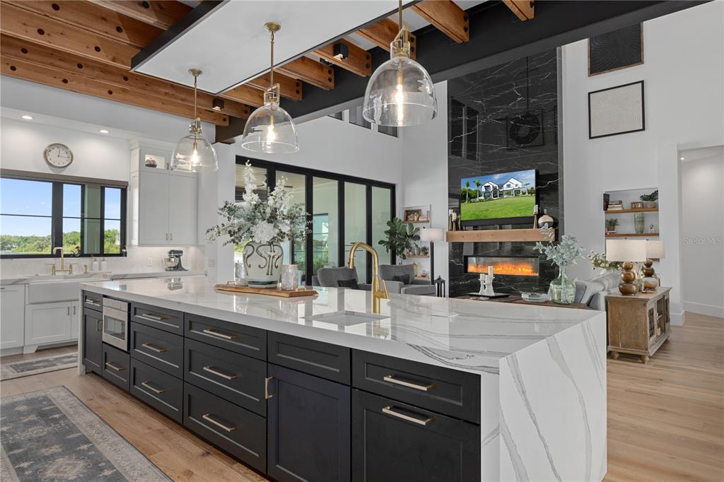 A modern kitchen features a large marble-topped island with dark cabinets and pendant lighting — 692 GLADWIN AVENUE, FERN PARK, FL