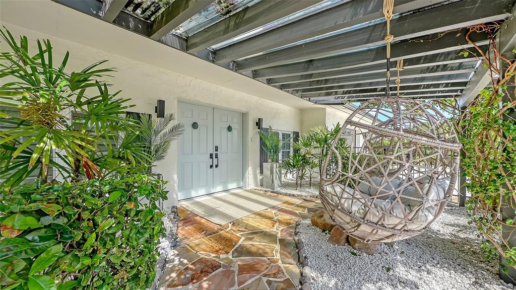 A covered patio features a stone walkway, a hanging egg chair, and lush green plants — 3624 S LOCKWOOD RIDGE ROAD, SARASOTA, FL