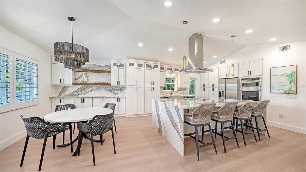 A modern kitchen features white cabinetry, a large marble island, and a dining area — 3624 S LOCKWOOD RIDGE ROAD, SARASOTA, FL