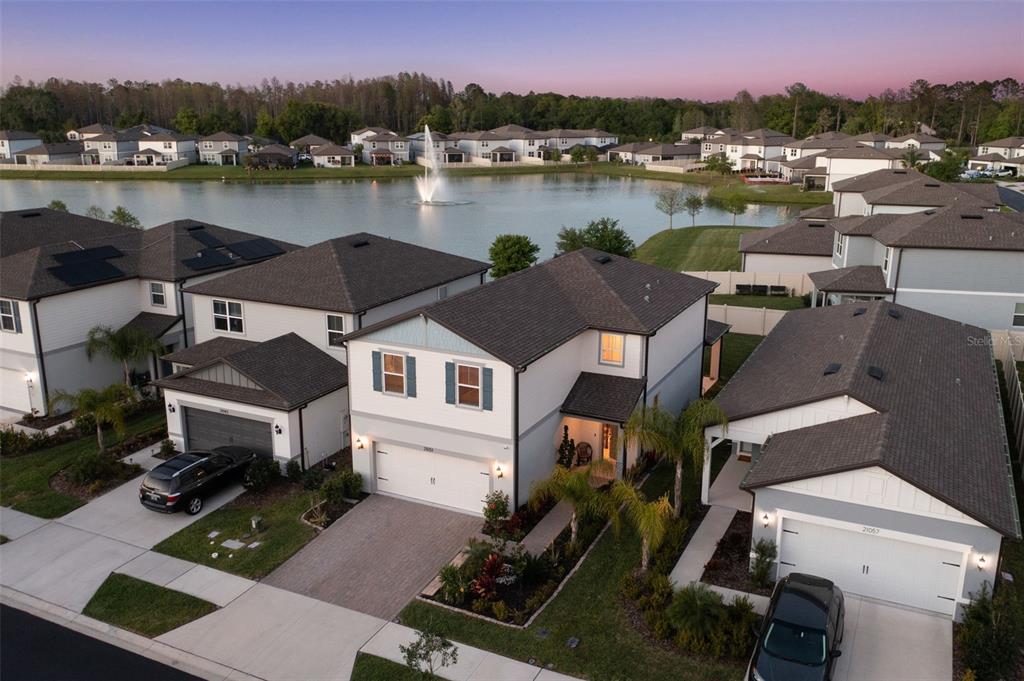 An aerial view of suburban houses with dark roofs situated near a lake with a fountain — 21051 MONZA LOOP, LAND O LAKES, FL
