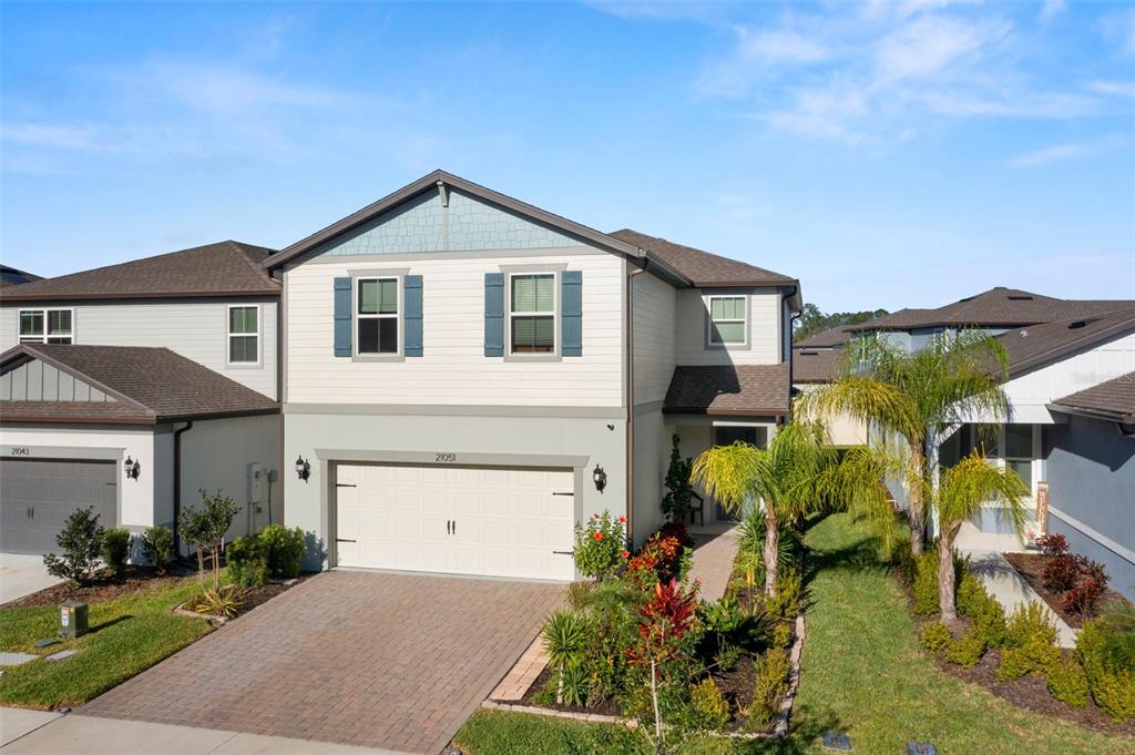 A two-story suburban house features a paved driveway, a two-car garage, and landscaped front yard — 21051 MONZA LOOP, LAND O LAKES, FL