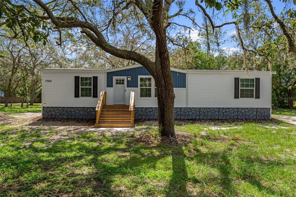 A single-story manufactured home with white siding, blue accents, and a wooden front staircase — 17912 GREENSBORO STREET, SPRING HILL, FL