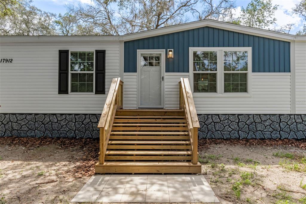 A single-story manufactured home with light siding and a stone-patterned foundation sits on a lot — 17912 GREENSBORO STREET, SPRING HILL, FL