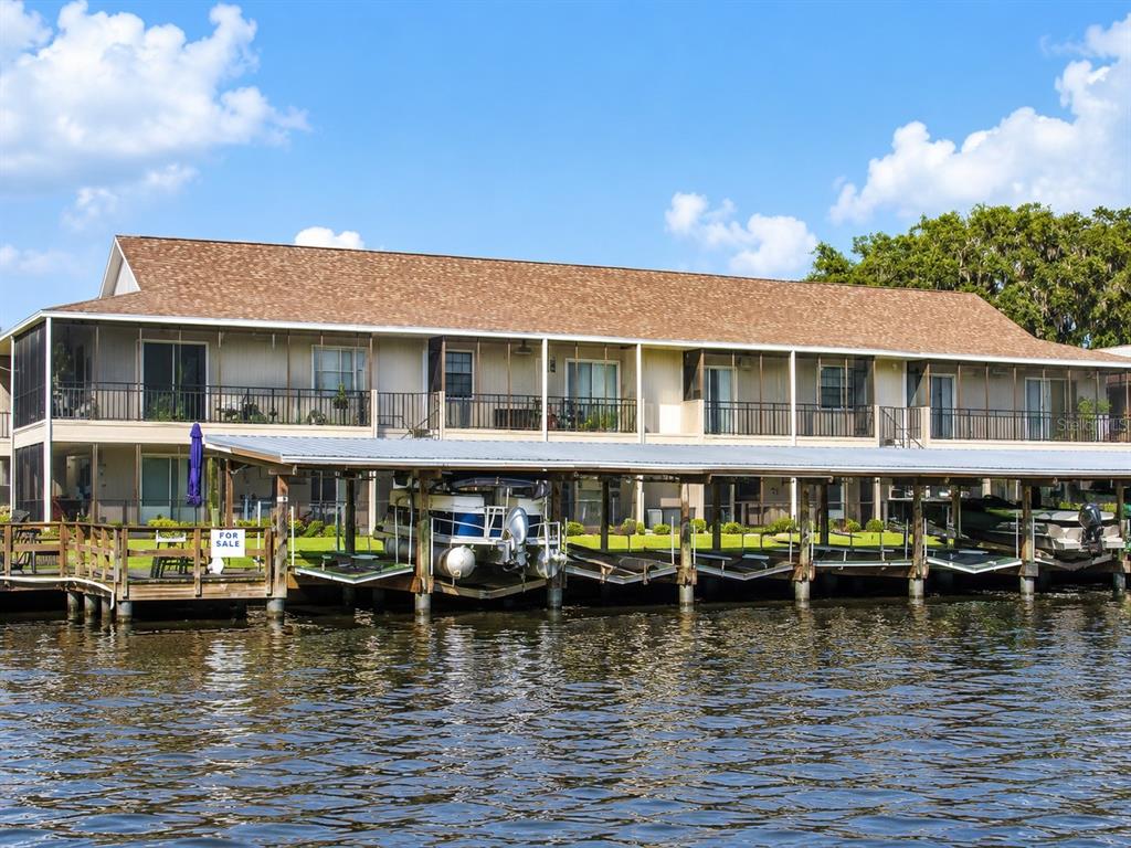 A two-story apartment building with screened balconies sits behind a covered boat dock on water — 1640 JUNO TRAIL UNIT 103F, ASTOR, FL