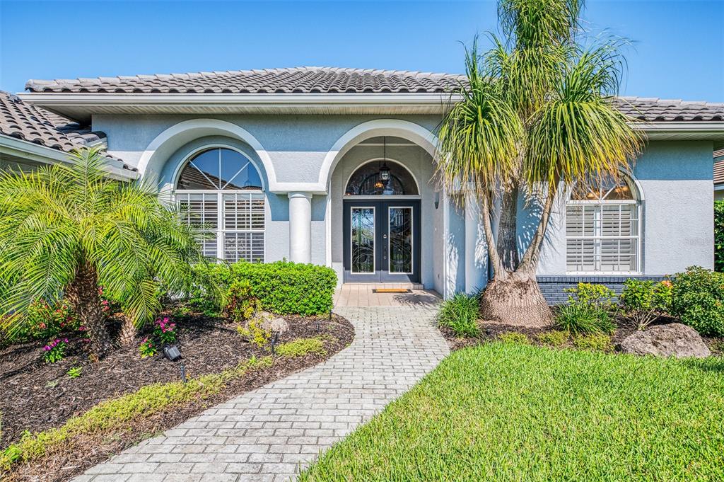 A paved walkway leads to the arched entryway and double front doors of a suburban home — 3615 PENNYROYAL ROAD, PORT CHARLOTTE, FL