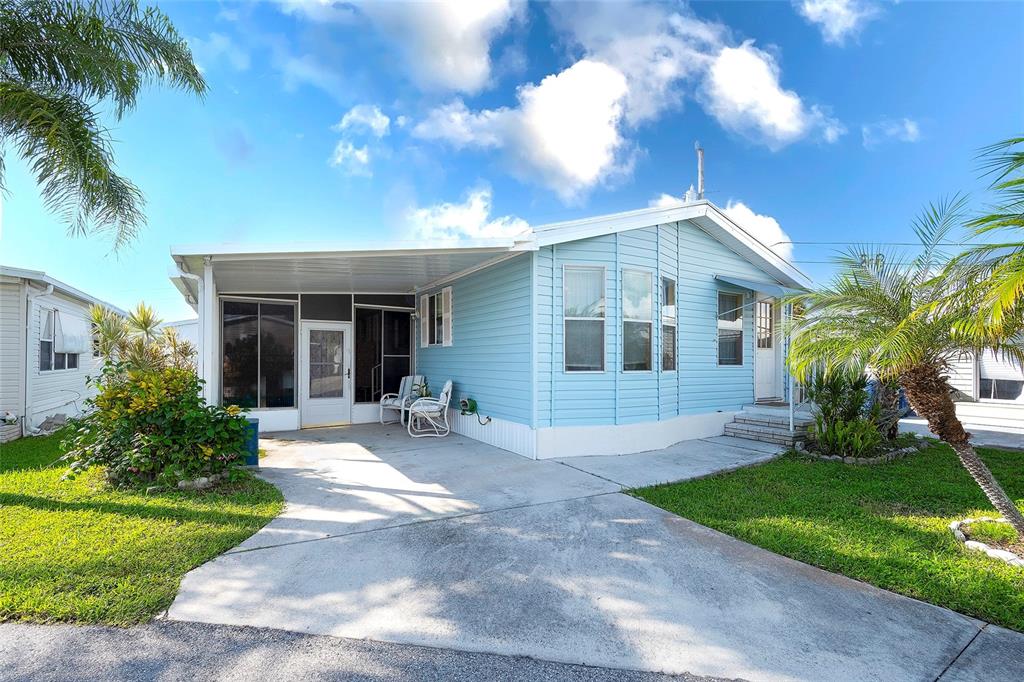 A light blue mobile home features a covered carport, a screened porch, and a front lawn — 2062 CHAMPION STREET, SARASOTA, FL