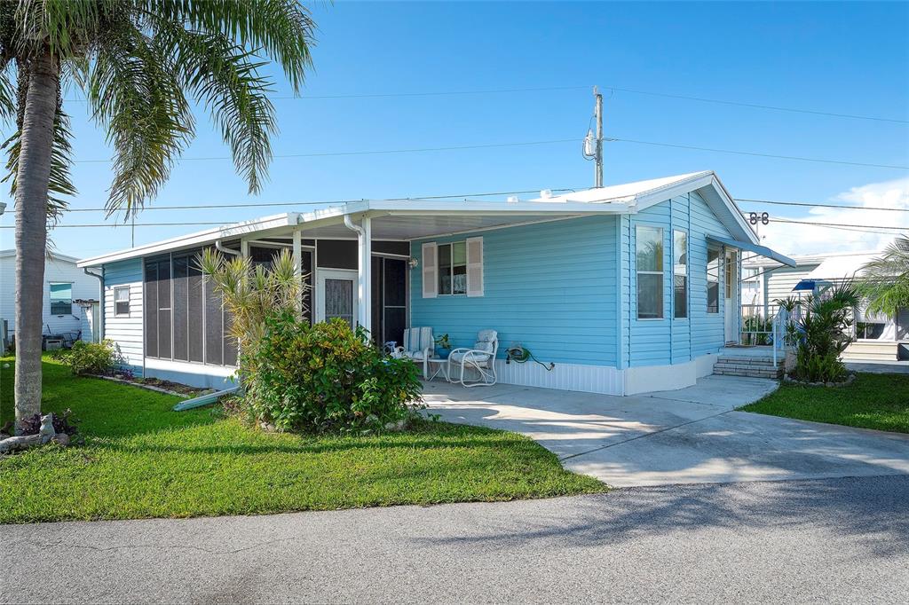 A light blue mobile home features a screened-in porch, a carport, and a palm tree — 2062 CHAMPION STREET, SARASOTA, FL
