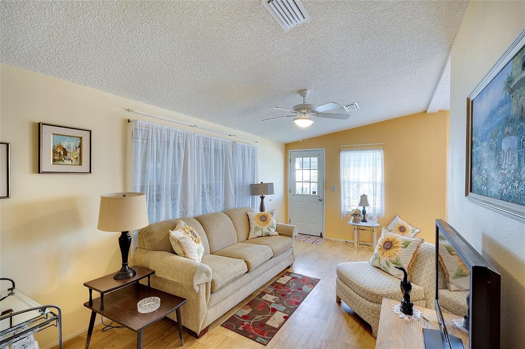 A living room with a beige sofa, patterned armchair, wood-look flooring, and a ceiling fan — 2062 CHAMPION STREET, SARASOTA, FL