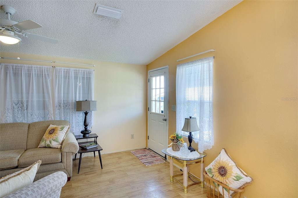 A living room features light yellow walls, wood-look flooring, a ceiling fan, and a white door — 2062 CHAMPION STREET, SARASOTA, FL