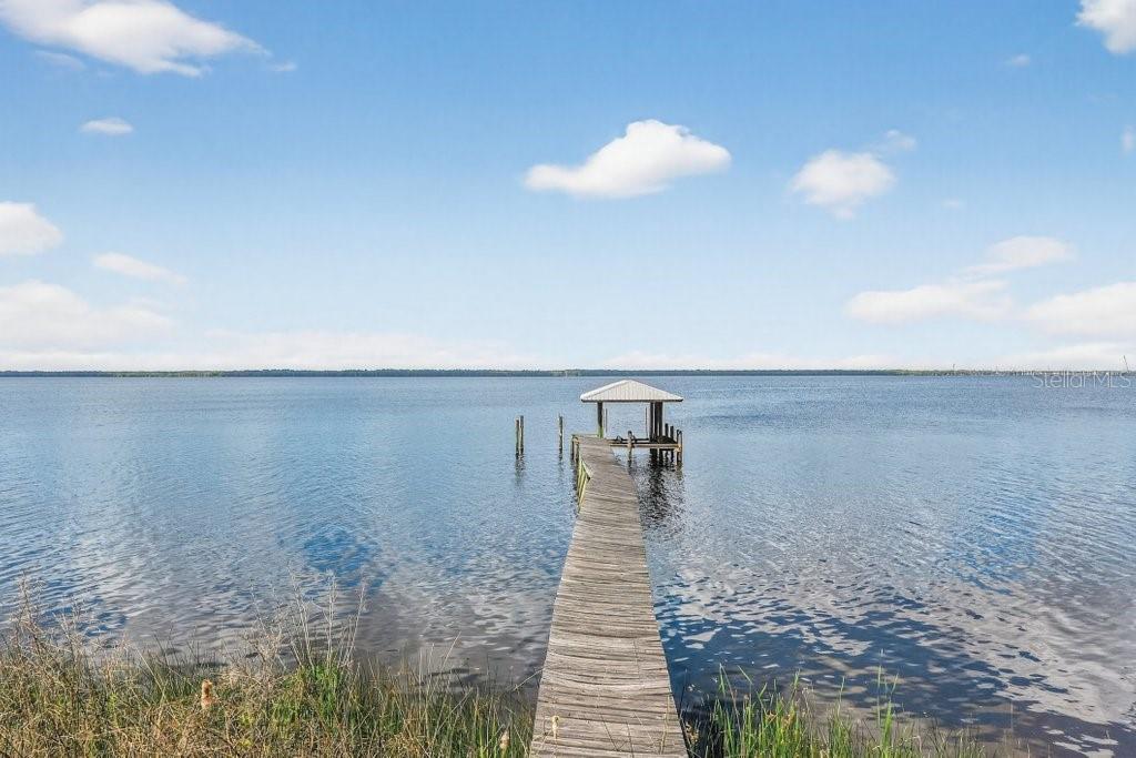 A wooden dock with a covered boat slip extends into a large, calm lake — 6373 JACK WRIGHT ISLAND ROAD, ST AUGUSTINE, FL
