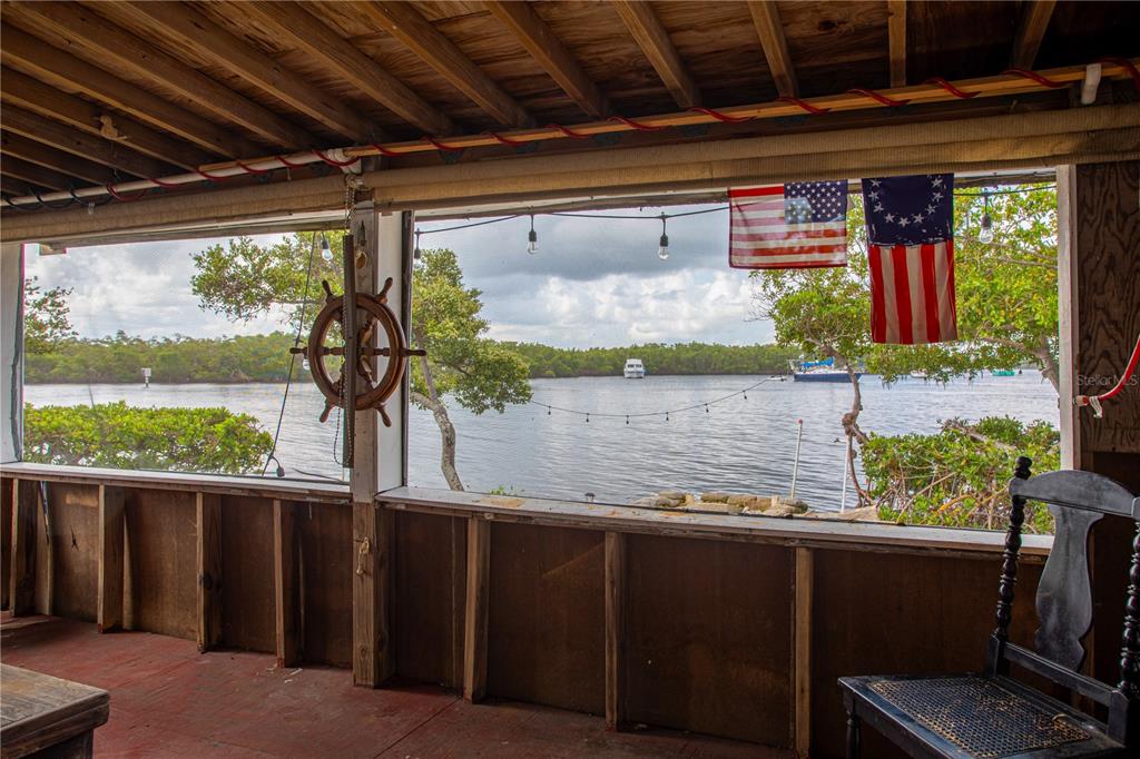 A screened-in porch features a wooden ship's wheel, American flags, and a view of water — 3312 W SHELL POINT ROAD, RUSKIN, FL